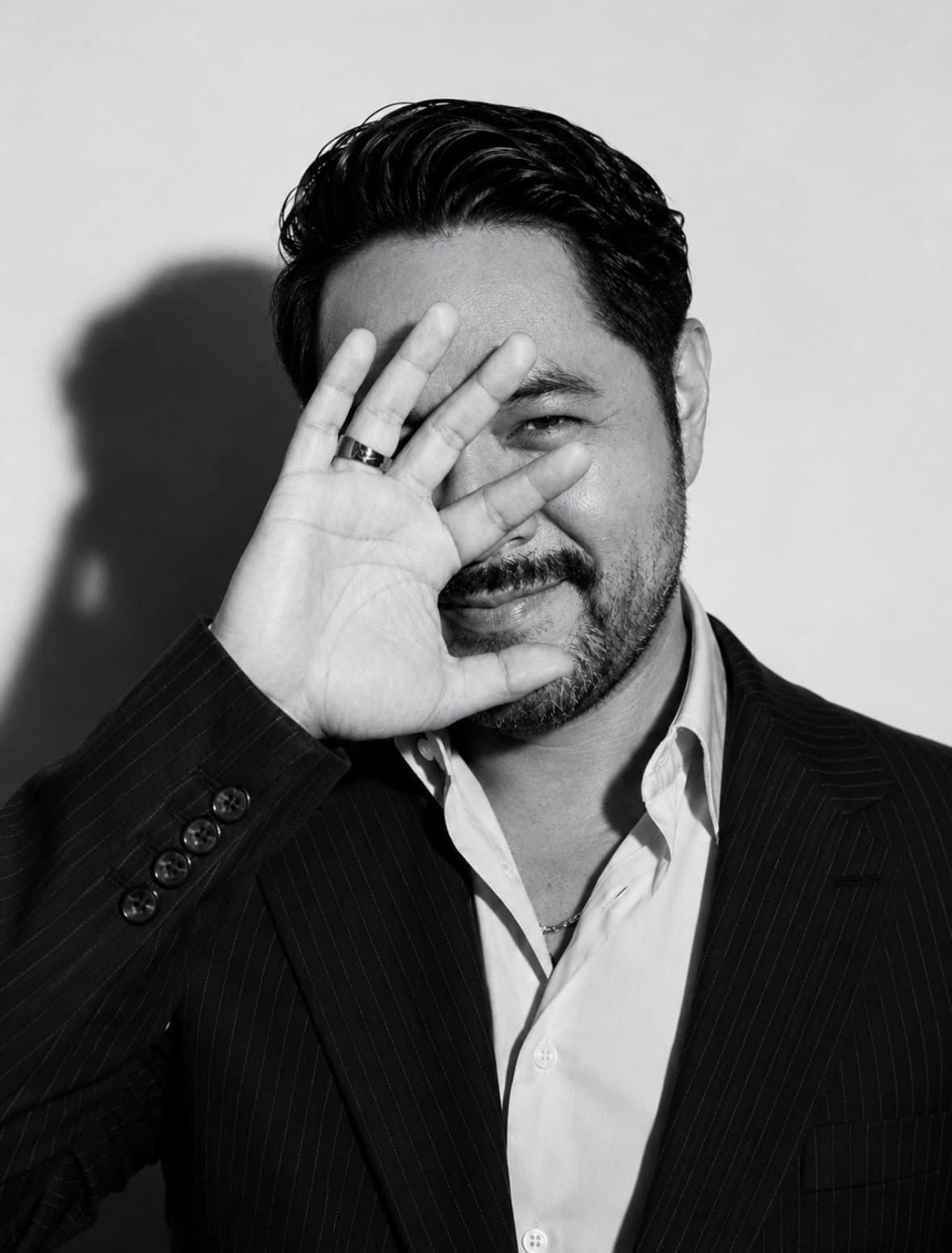 Black-and-white editorial portrait of Eduardo Ramos, hand raised in front of his face